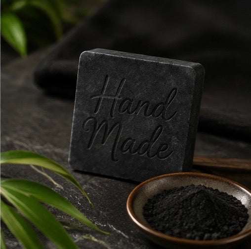Charcoal Soapbar in a dark charcoal-gray square bar with a textured surface and raised Hand Made lettering